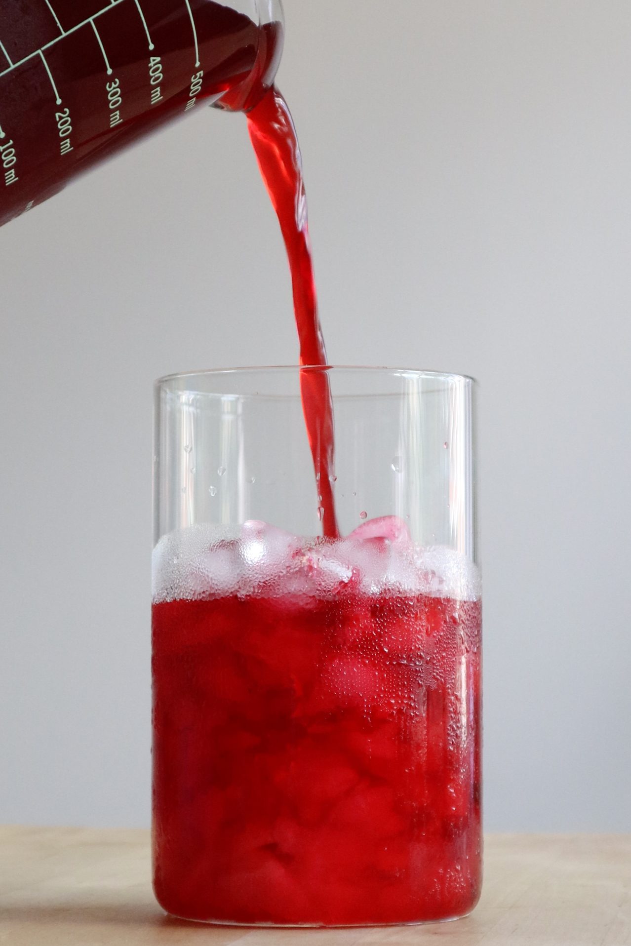 Pouring brewed hibiscus tea over ice into a glass