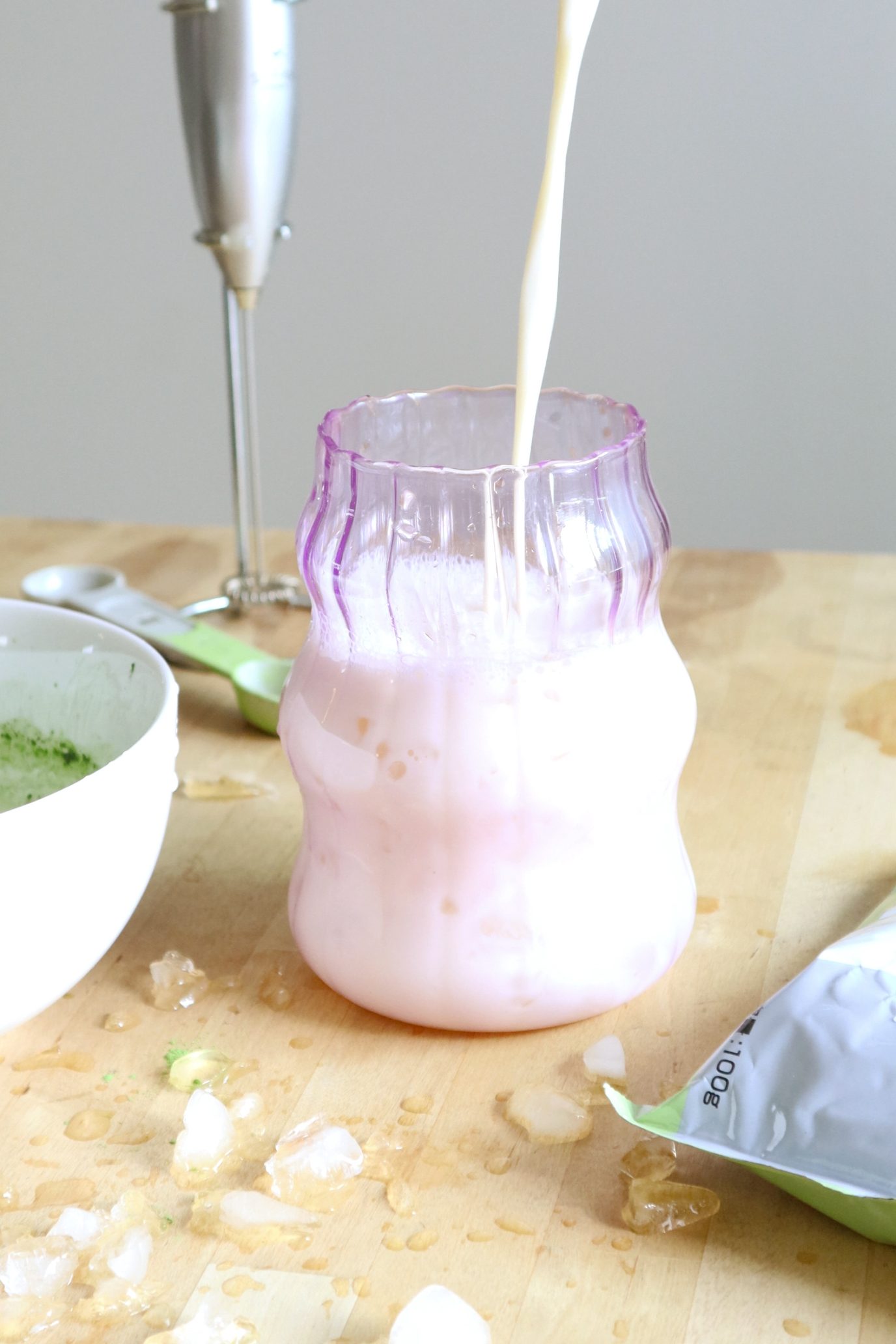 Pouring oat milk into a glass to make a matcha latte