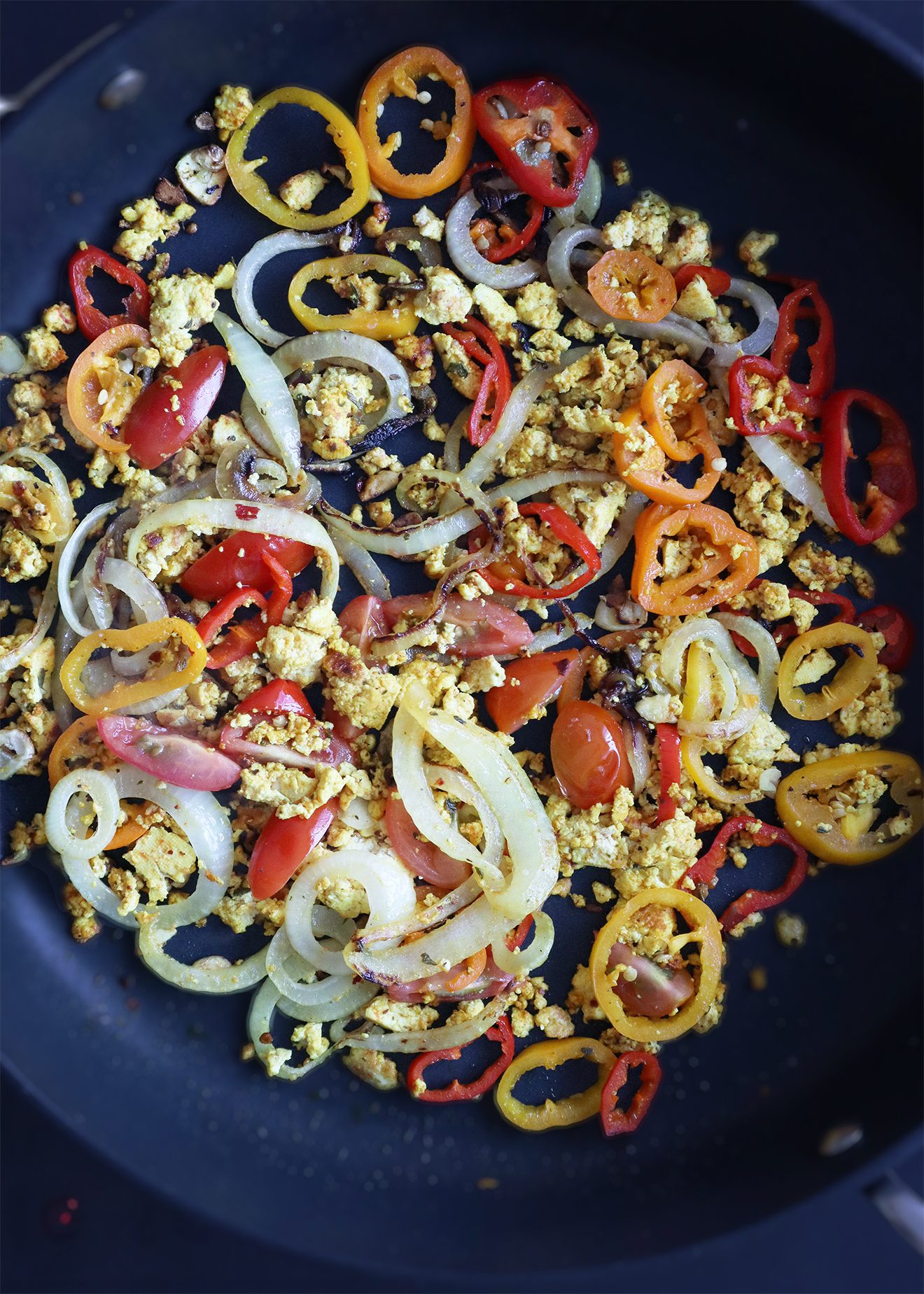 Vegan scrambled tofu with peppers, onions, and tomatoes cooking in a pan